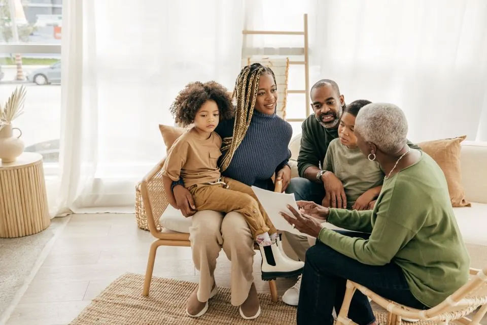 A family with young daughter talk with an advisor on the couch at home.